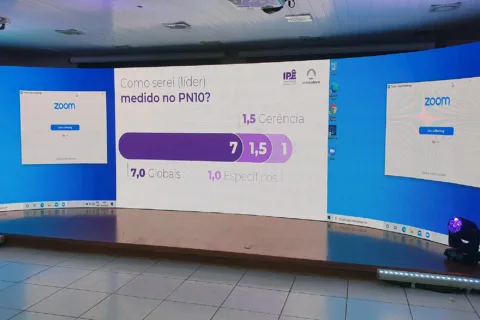 Painel de LED curvo exibindo apresentação e participantes remotos em evento híbrido corporativo